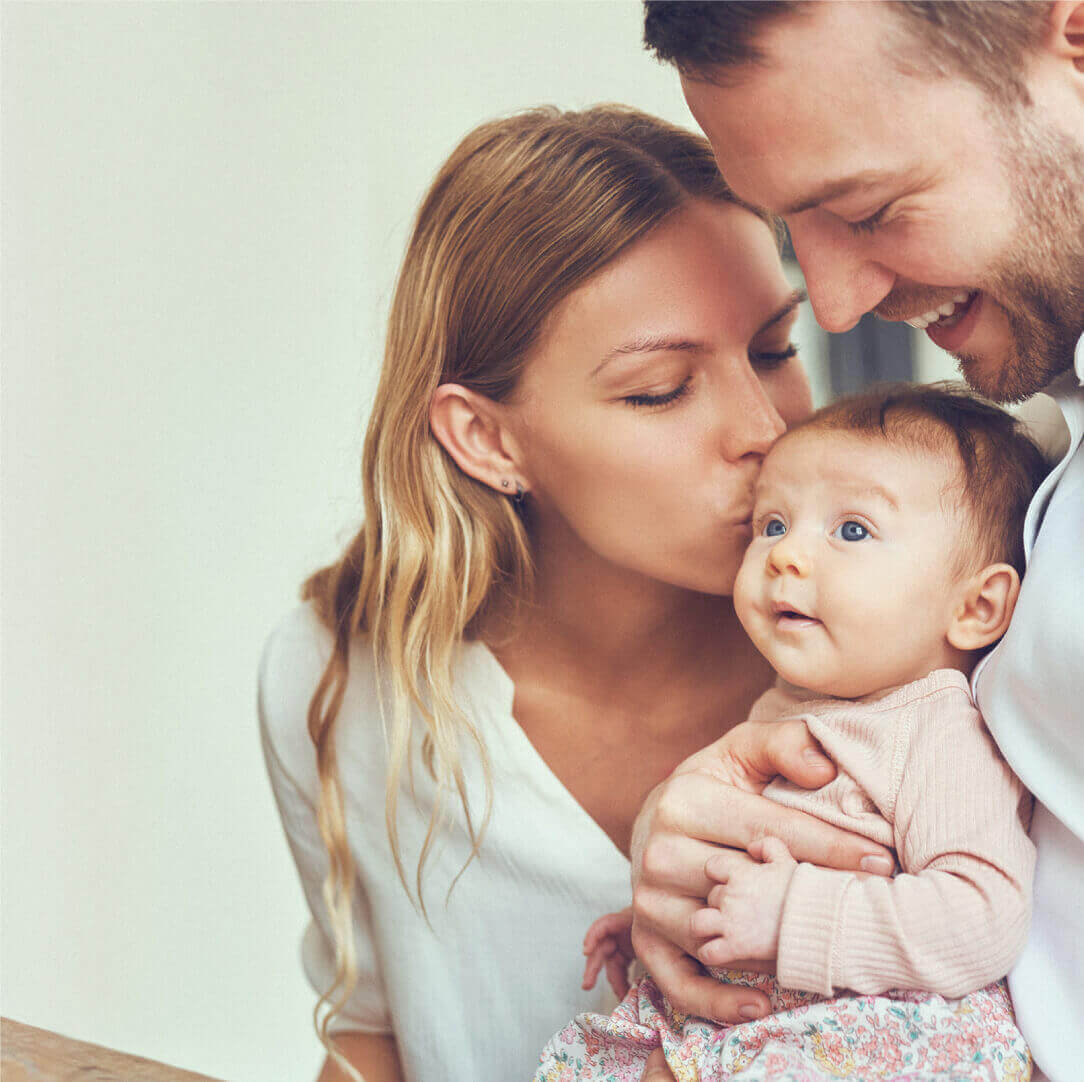 A happy couple kissing their baby