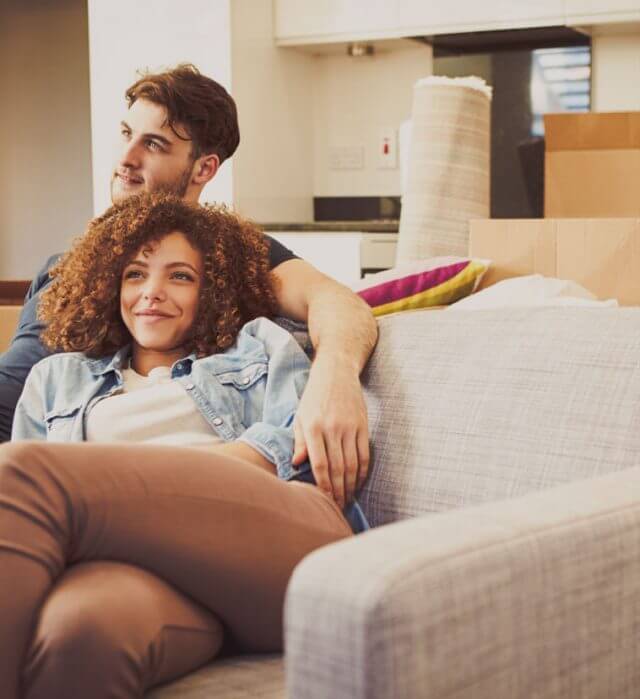 A happy couple relaxing on the sofa after buying a house and getting out of renting